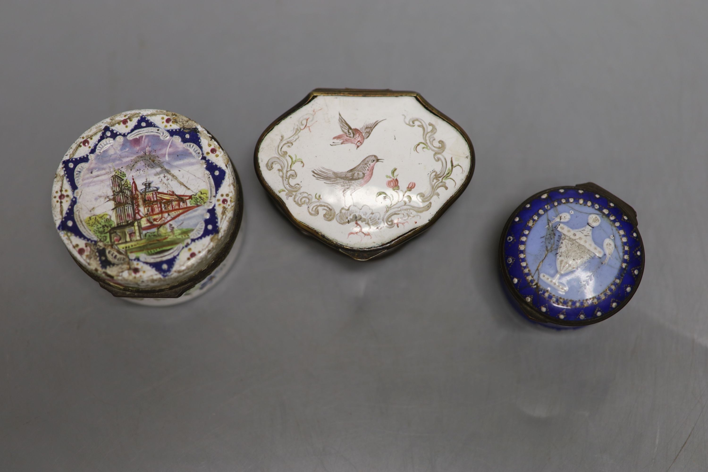 An 18th century white enamelled box painted with a palace, 5cm., a cartouche shaped box decorated with a birds, 6cm. and a patch box de